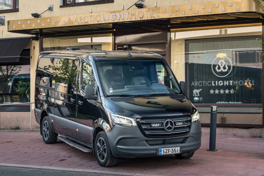Musta Mercedes-Benz Sprinter -tila-auto hotellin edessä