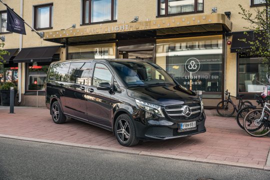 Musta Mercedes-Benz V -tila-auto hotellin edessä