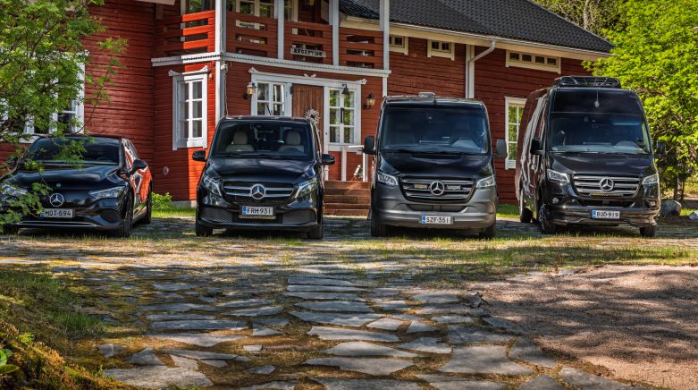 Henkilöauto, kaksi tila-autoa ja pikkubussi rivissä hirsitalon edessä